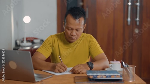 Student adult Asian man using laptop and writing on notebook. Learning, exam and education concept.