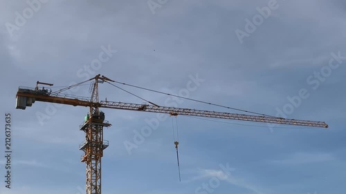 Tall yellow tower crane with lattice mast and extended jib set against a clear blue sky. The hook and cable system highlight construction engineering, making this image ideal for architecture theme. 