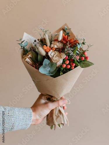 Hand holding flower bouquet, floral gift concept, autumn bouquet, kraft paper wrap, close up hand