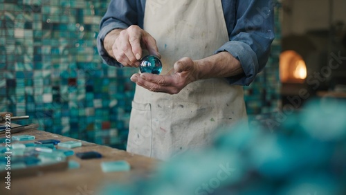 Craftsman handling a blue glass piece in a workshop with vibrant tiled wall