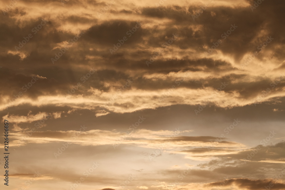 Fototapeta premium Dramatic clouds in the sky tinted with golden sunset colors after a heavy afternoon rainstorm