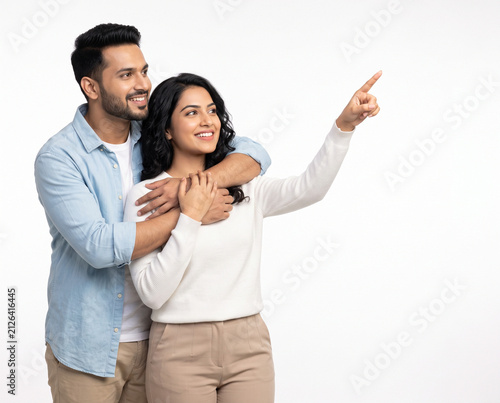 Young Indian couple embracing while pointing toward copy space on a white background for future planning investment success and lifestyle advertising