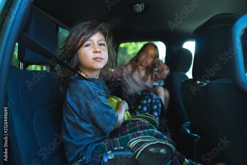 Two boys sitting in the back seat of a car with bags and blankets