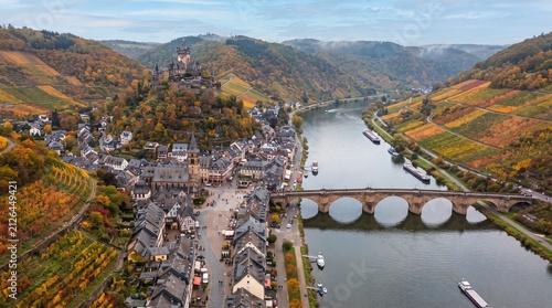 Aerial view of a charming European village nestled in a river valley with vineyards in autumn colors a historic castle on a hill and a stone bridge perfect for travel and landscape themes
