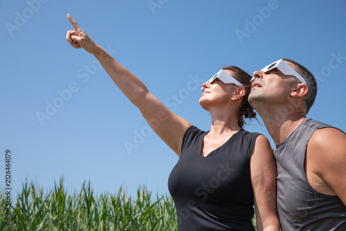 Fotografía Medium close-up profile view of a woman and a man wearing protective paper glasses, looking up into the sky to observe the upcoming solar eclipse on August 12, 2026