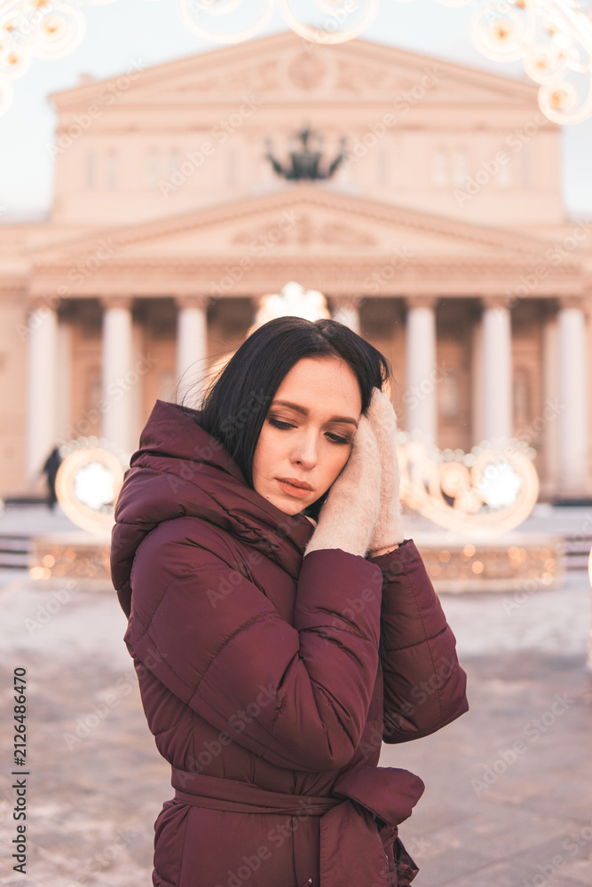 Fototapeta premium Woman in maroon coat standing in Moscow with Christmas lights, building in background. Winter holiday concept with decoration.
