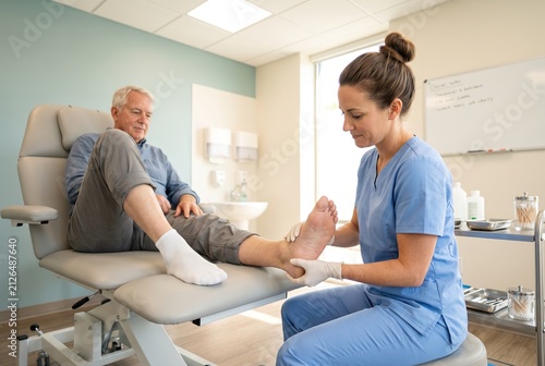 A medical professional is examining a patient's foot in a clinic. The patient is sitting on an exam table. The professional wears gloves while providing care