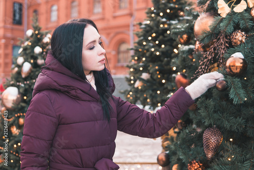 Photography Woman touching Christmas tree decoration on snowy Moscow street