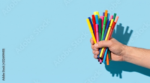 Hand Holding Bunch of Colorful Markers on Blue Background