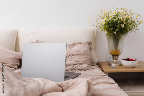 Konstfotografi Cozy minimalist bedroom with an open laptop on a soft bed beside fresh flowers,