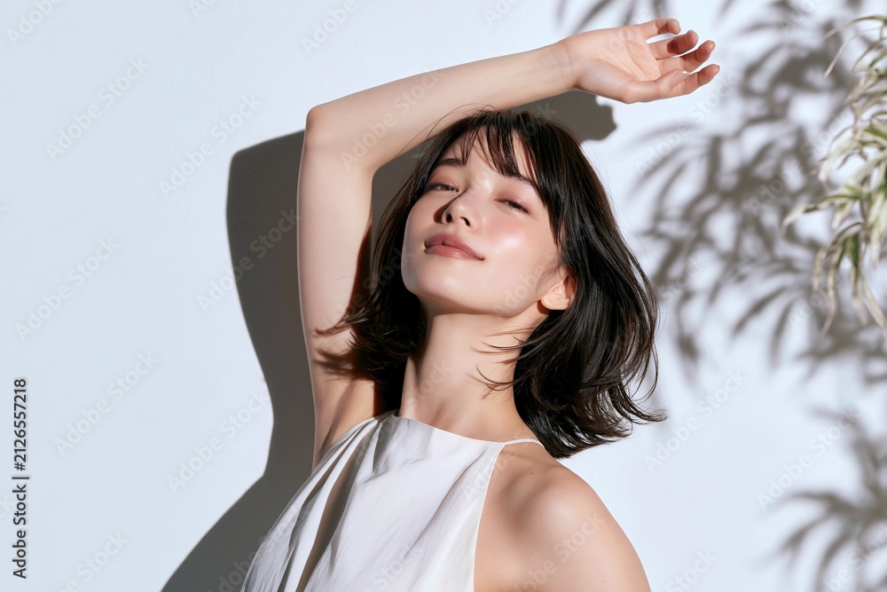 Naklejka premium 木漏れ日が美しい白い壁の前で穏やかな表情を見せる日本人女性
