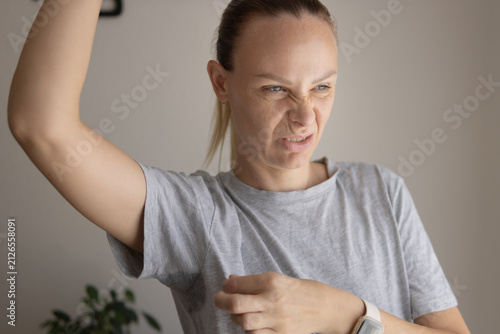 Bild auf Leinwand Woman noticing unpleasant underarm odor, expressing disgust at perspiration and