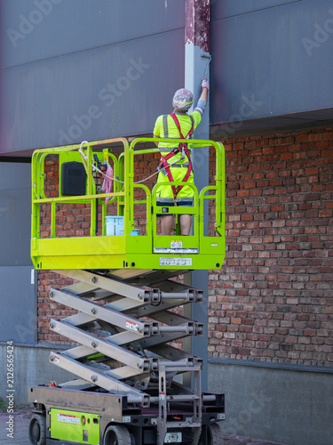 Construction Worker Painting Steel Support Column from Elevated Scissor Lift at Building Exterior Site