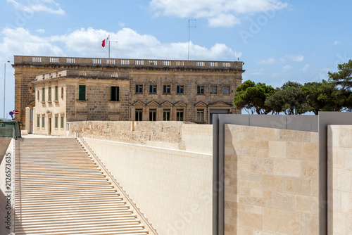 Modern stone panels and steps lead toward a the Central Bank of Malta with a Maltese flag flying above, Valletta