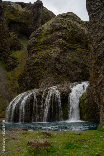 Fotografie Beautiful Stjornarfoss cascade waterfall with blue water pool and green mossy rocks, Icelandic landscape