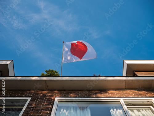 Foto A white flag with a red heart waves on a pole atop a modern brick building against a blue sky