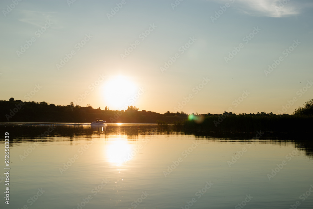 Obraz premium Motorboat cruising across a calm lake at golden sunset with reflections