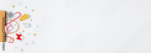 Gift bag with tiny presents, golden and silver decorations, candy canes on white background. Ideal for holiday banners, winter festive sales and Christmas promo layouts. Flat lay, copy space.