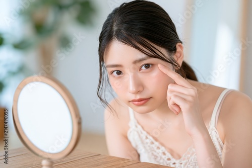 美容に気を遣う若い女性が鏡で目元を指差し肌を確認するシーン