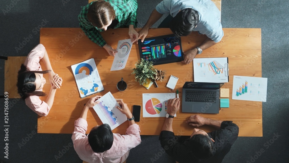 Fototapeta premium Top down view of businesswoman explain and present financial chart. Diverse group discuss and listening presentation about stock market statistic at meeting table with investment graph. Convocation.