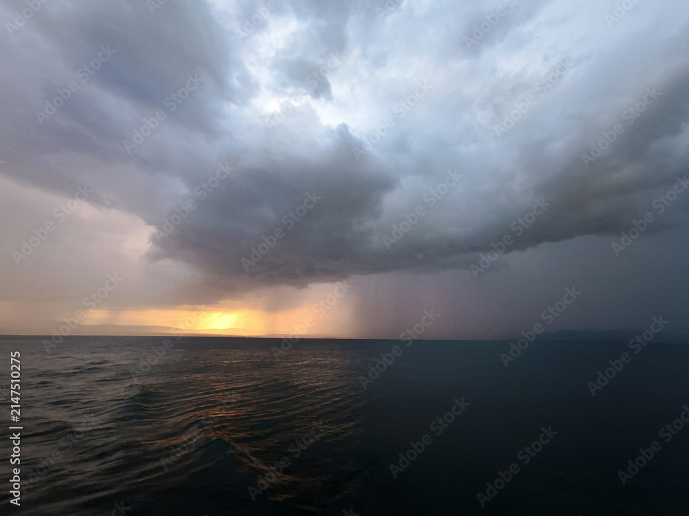 Fototapeta premium Dramatic Thunderstorm Over the Sea with Rain Curtain and Glowing Sunset Horizon