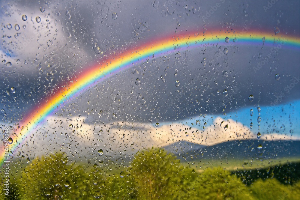 Obraz premium Rainbow arching over wet window and green landscape