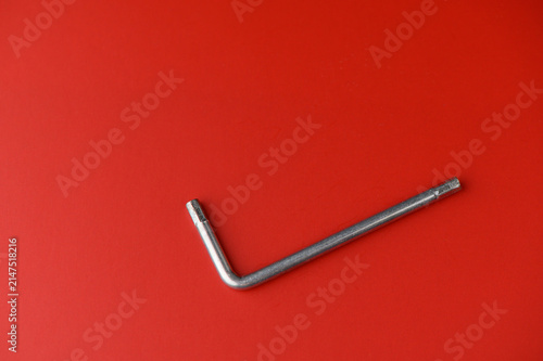 Bild auf Leinwand The picture captures a metal tool laid out flat against a bold red surface, highlighting its distinctive L-shape and shiny finish