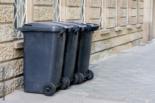 Three gray residual waste bins stand against a stone building wall in a German city