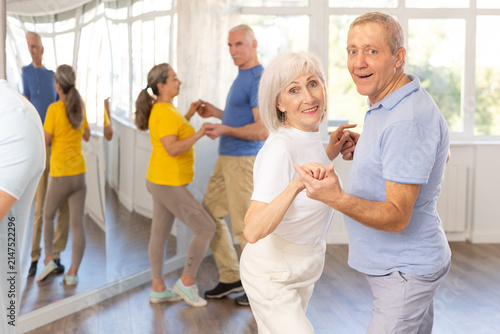 Group of happy elderly pensioners learning to dance latin dances in dance studio
