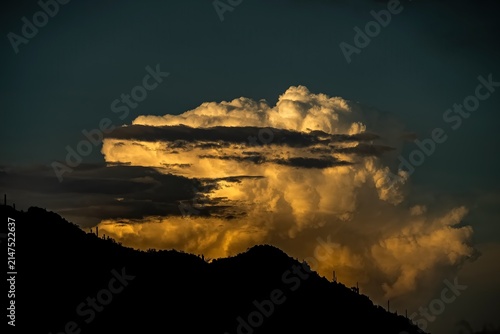 Quadro su tela Glowing monsoon storm cloud over a silhouetted desert mountain ridge
