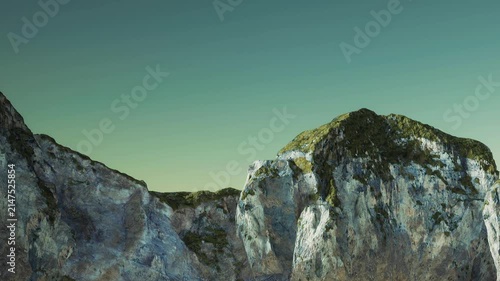 A large rock formation shows rugged surfaces and green vegetation. The clear sky adds brightness to the scene. This rocky coastal area is unpopulated and natural.