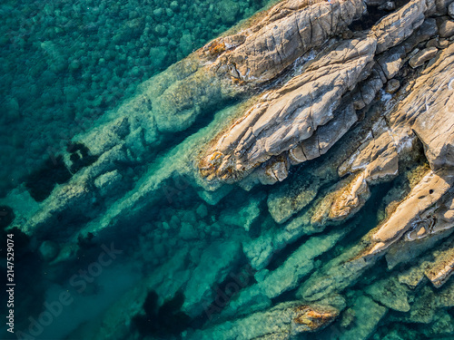 Top down aerial shot of natural rock formation underwater showing clear transparent sea with turquoise hues and rock texture in Liguria Italy
