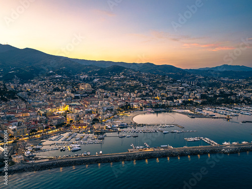 Aerial drone view of Sanremo cityscape and hills featuring the brightly illuminated Sanctuary of Madonna della Costa during twilight sunset in Liguria Italy
