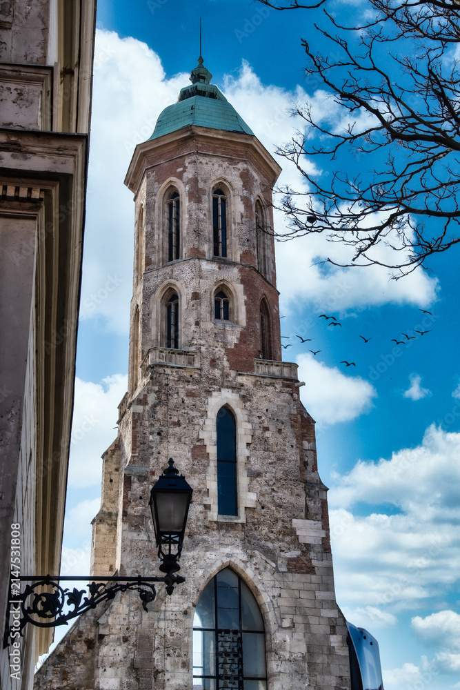 Obraz premium Historical tower stands tall against the blue sky with birds flying nearby in a city setting during the day