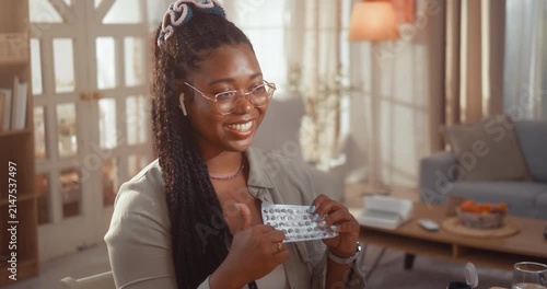 Young Black woman shows a blister pack of pills to a female doctor during a telemedicine video call consultation from home.