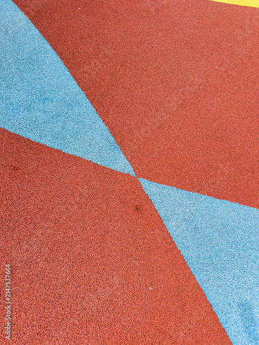 Brightly colored playground surface shows red and blue sections meeting at an angle during daytime