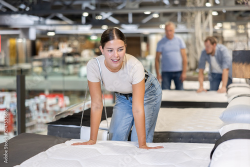 Foto In furniture store, girl examines bed and mattress