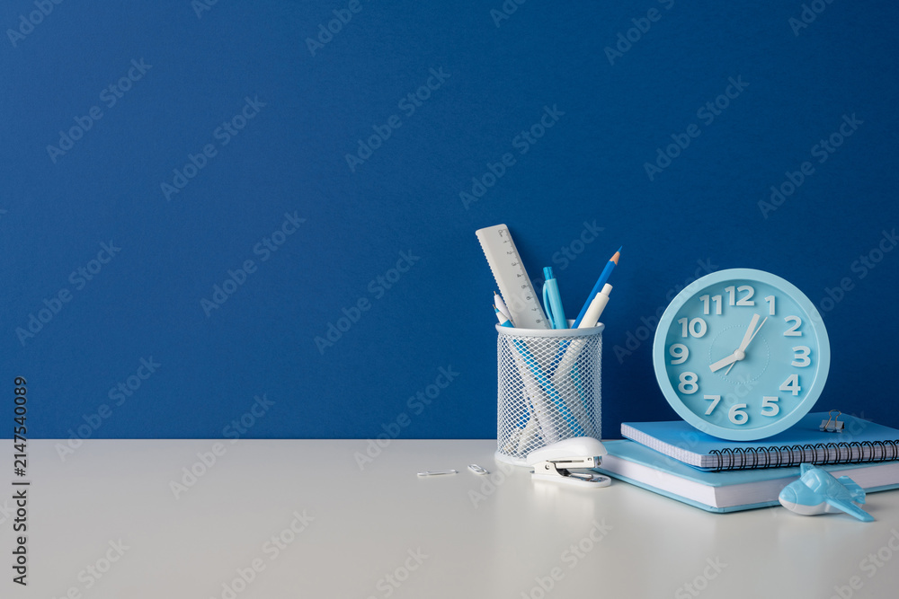 Obraz premium Side view photo of back to school stationery and blue alarm clock on desk