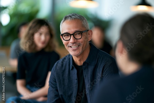 Business collaboration and team meeting smiling mature man in glasses talking with colleagues in a modern office