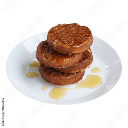 Fotografie A tall stack of thick, golden-brown round waffles served on a white plate, generously drizzled with glossy honey or maple syrup pooling at the base