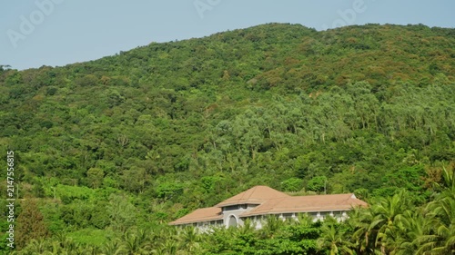 Landscape of green mountains covered by trees and plants filmed at sunny day and lonely hotel built on the slope. Scenery of tropical nature with its hills and bushes on the cliffs. Environment theme.