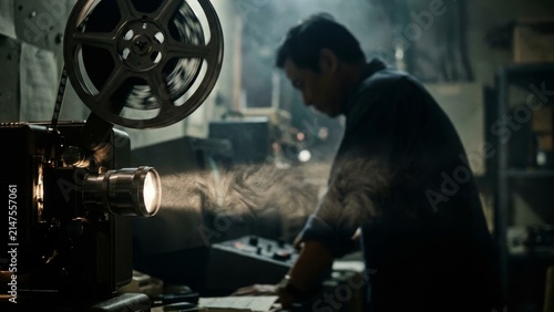 Entertainment - Asian projectionist operating vintage film projector in dark room