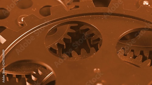 Extreme macro shot looking through the circular cutout of a foreground bronze cogwheel to reveal meshing metallic gear teeth, symbolizing precision engineering, complex systems, teamwork, and warm-ton