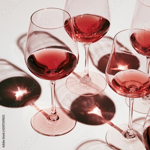 Wine glasses contain varied amounts of red liquid against a white backdrop.