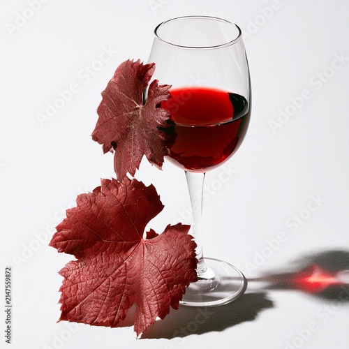 Red wine glass with grape leaves sits on a white background under soft shadow with a clipping path included.