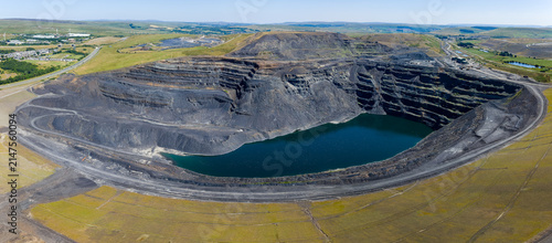High angle panoramic view over closed opencast coal mine pit, dark water gathered at bottom of terraced rock face, former mining site pending land restoration