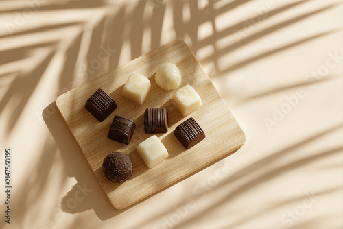 Assorted dark and white chocolate pralines on a wooden board with tropical shadows