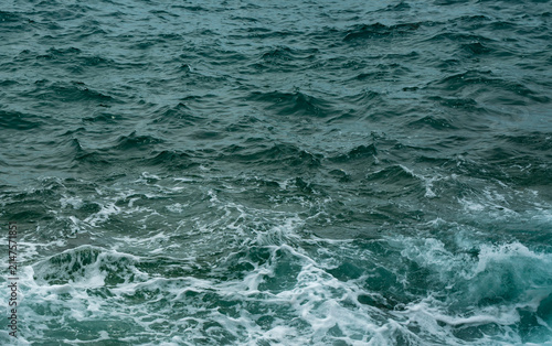 Dark turquoise sea water surface with ripples and white foam