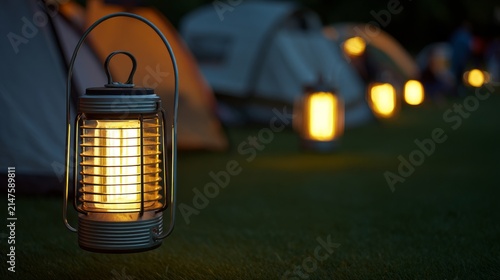 At dusk, the camping tents on the green grass are illuminated by local industrial outdoor lights, with a close-up shot of the warm light.