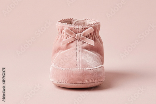 Dusty pink velvet baby bootie or slipper with a bow on a matching background